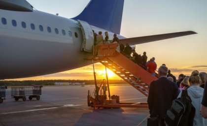 people in a line going up stairs to a plane door with the sun setting in the background
